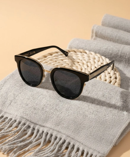 White Angel luxury black and gold sunglasses on a grey wool scarf and woven background.