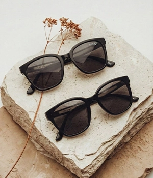 White Angel black square sunglasses with dark lenses on a natural stone surface.